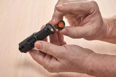 Hands hold a small black flashlight and replace the battery in it Foto stock