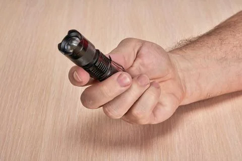 Hands hold a small black flashlight aimed at the diagonal of the frame Stock Photos