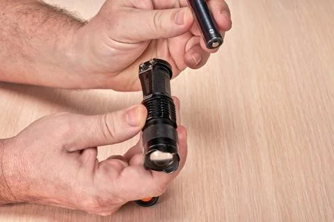 Hands hold a small black flashlight and replace the battery in it Stock Photos