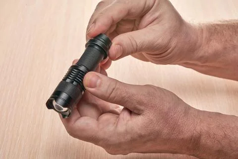 Hands hold a small black flashlight to replace the used battery Stock Photos