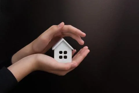 Hands hold a small model of the house in both palms on a black background Stock Photos