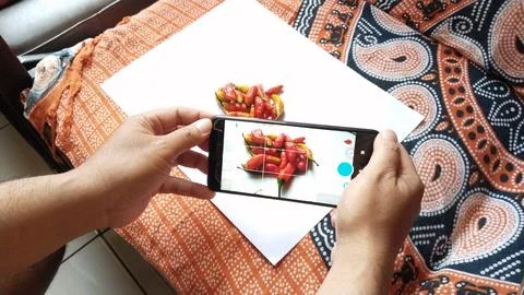 Hands hold a smartphone capturing a vibrant flat lay of red and yellow chili  Stock Photos
