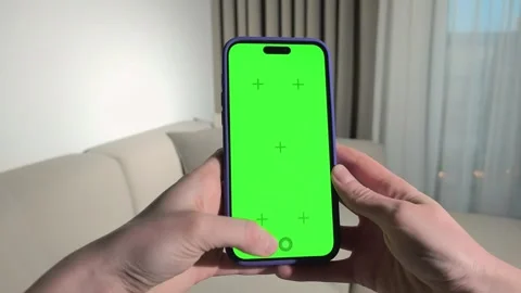 Hands hold a smartphone with green screen in a living room. Thumb taps the .. Stock Footage 340283938