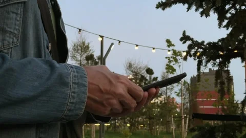 Hands hold a smartphone, typing a message outdoors in the evening. String l.. Stock Footage 338398000