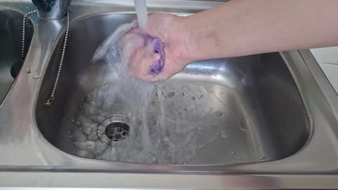 Hands hold a sponge and rinse it under running water in a kitchen sink Stock Footage 344260162