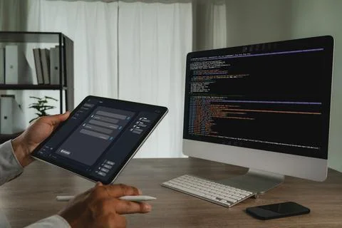 Hands hold a tablet showing an AI chatbot interface beside a desktop comput.. Foto stock