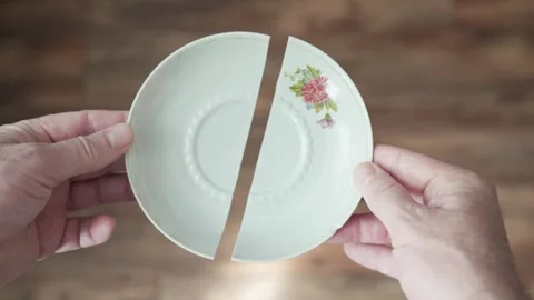 Hands hold two halves of a broken porcelain plate Stockbeeldmateriaal 342135433