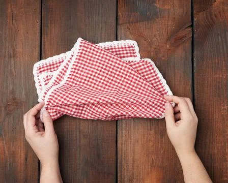 Hands hold white red checkered kitchen towel on a brown wooden background ... Stock Photos