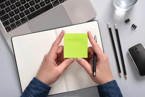 Hands holding a blank sticky note in green over an open notepad on a table. A Stock Photos