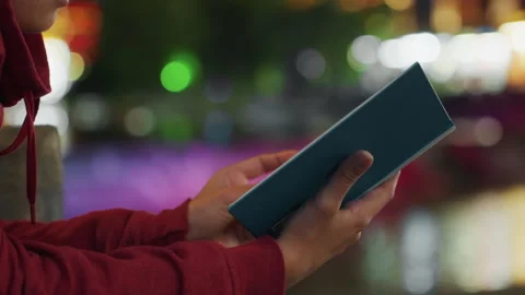 Hands holding blue journal at night, city lights blur into colorful bokeh Stock Footage 345523065