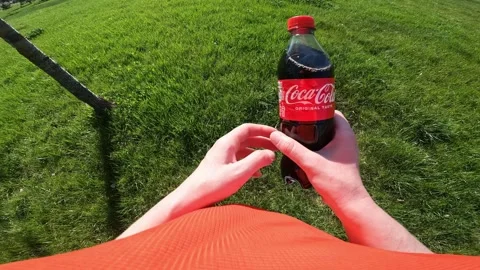 Hands holding a bottle of Coca-Cola on a green grass background Stock Footage 334322721