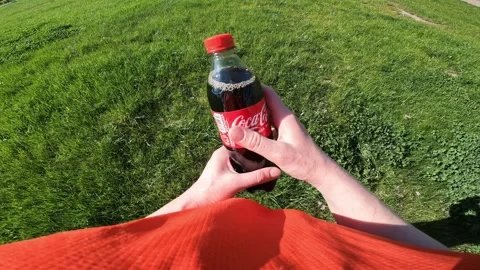 Hands holding a bottle of Coca-Cola on a green grass background Stock Footage 334322724