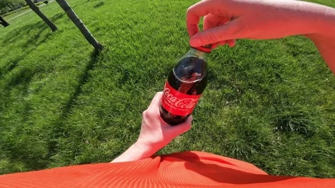 Hands holding a bottle of Coca-Cola on a green grass background Stock-Footage 334322727