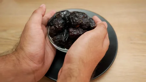 Hands Holding Bowl of Dark Dates on Black Plate Stock Footage 320726178