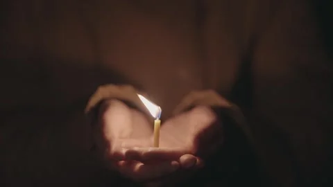 Hands holding a candle with a burning flame during a moment of reflection Stock Footage 329912595