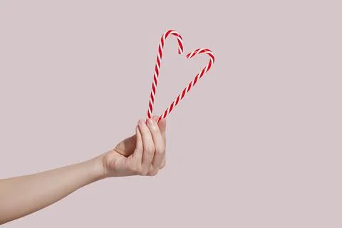 Hands holding candy canes in the shape of heart on pink background. Charity Stock Photos