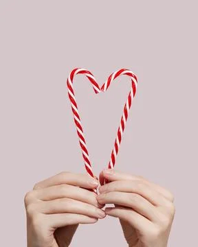 Hands holding candy canes in the shape of heart on pink background. Charity Stock Photos