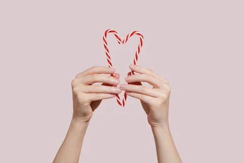 Hands holding candy canes in the shape of heart on pink background. Charity Stock Photos