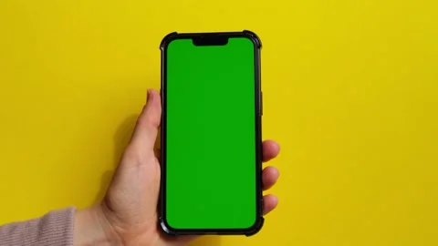 Hands holding cell phone with green screen on yellow background. Chroma key Mock Stock Footage 221468771