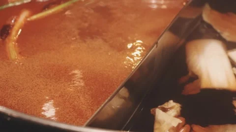 Hands holding chopsticks dipping a slice of pork into a bubbling shabu-shab.. Stock Footage 343613750