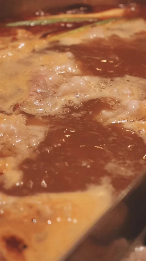 Hands holding chopsticks dipping a slice of pork into a bubbling shabu-shab.. Stock Footage 343613771