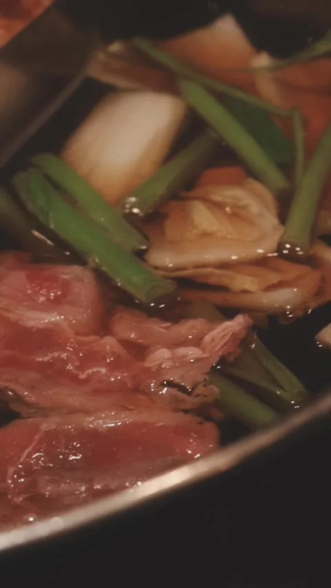 Hands holding chopsticks dipping a slice of pork into a bubbling shabu-shab.. 스톡 동영상 343613772