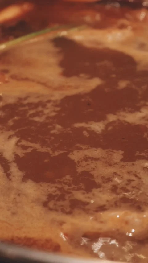 Hands holding chopsticks dipping a slice of pork into a bubbling shabu-shab.. Stock Footage 343613773