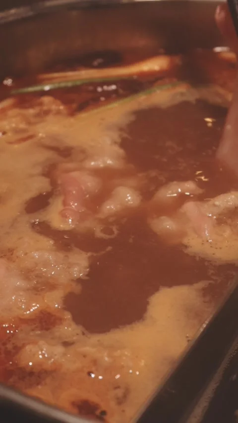 Hands holding chopsticks dipping a slice of pork into a bubbling shabu-shab.. Stock Footage 343613774