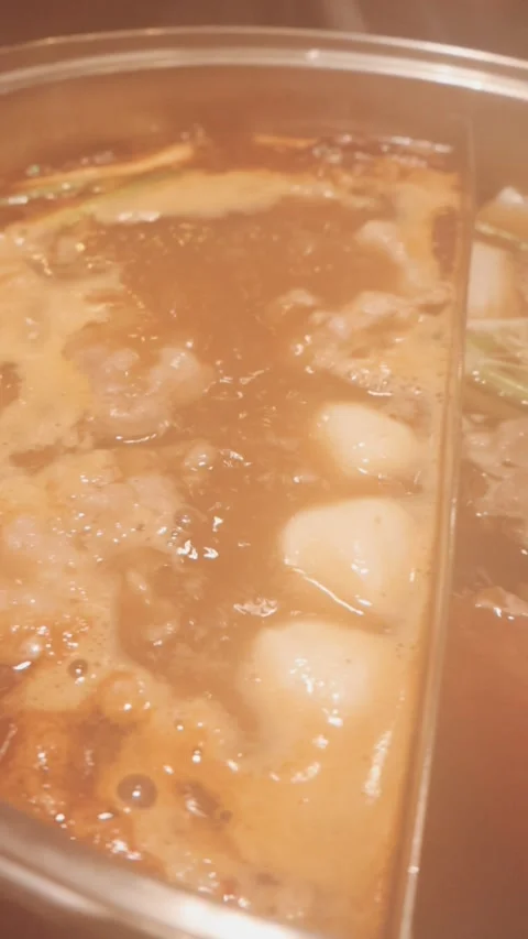 Hands holding chopsticks dipping a slice of pork into a bubbling shabu-shab.. Stock Footage 343613806