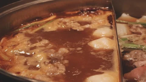 Hands holding chopsticks dipping a slice of pork into a bubbling shabu-shab.. Stock Footage 343613833