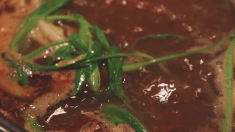 Hands holding chopsticks dipping a slice of pork into a bubbling shabu-shab.. Vidéo 343613834