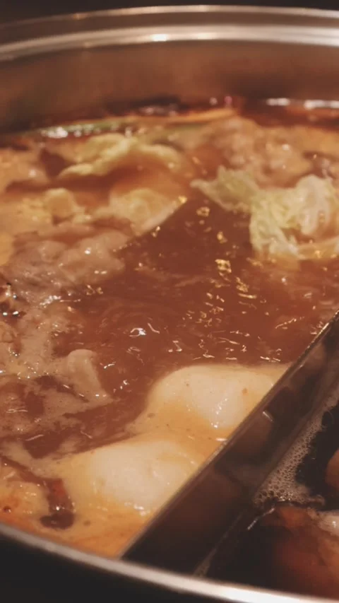 Hands holding chopsticks dipping a slice of pork into a bubbling shabu-shab.. Stock Footage 343613835