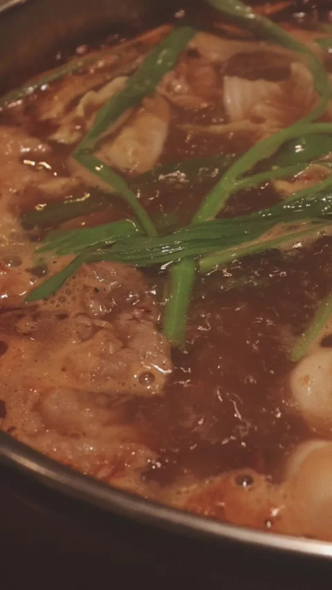Hands holding chopsticks dipping a slice of pork into a bubbling shabu-shab.. Stock Footage 343613845