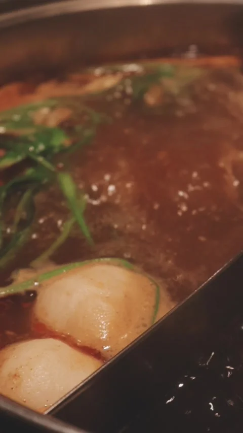 Hands holding chopsticks dipping a slice of pork into a bubbling shabu-shab.. Stock Footage 343613865
