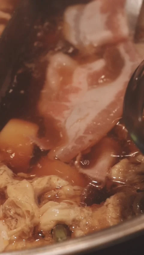 Hands holding chopsticks dipping a slice of pork into a bubbling shabu-shab.. Stock Footage 343613866