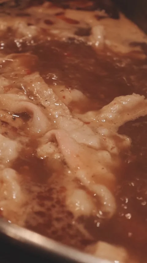 Hands holding chopsticks dipping a slice of pork into a bubbling shabu-shab.. Stock Footage 343613878