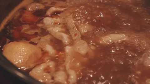 Hands holding chopsticks dipping a slice of pork into a bubbling shabu-shab.. Stock Footage 343613884