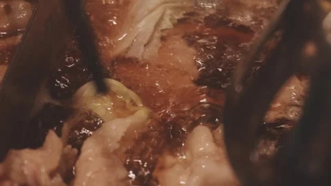 Hands holding chopsticks dipping a slice of pork into a bubbling shabu-shab.. Stock Footage 343613897