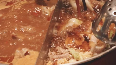 Hands holding chopsticks dipping a slice of pork into a bubbling shabu-shab.. Stock Footage 343613919