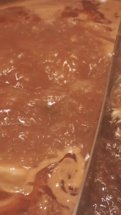 Hands holding chopsticks dipping a slice of pork into a bubbling shabu-shab.. Stock Footage 343613933