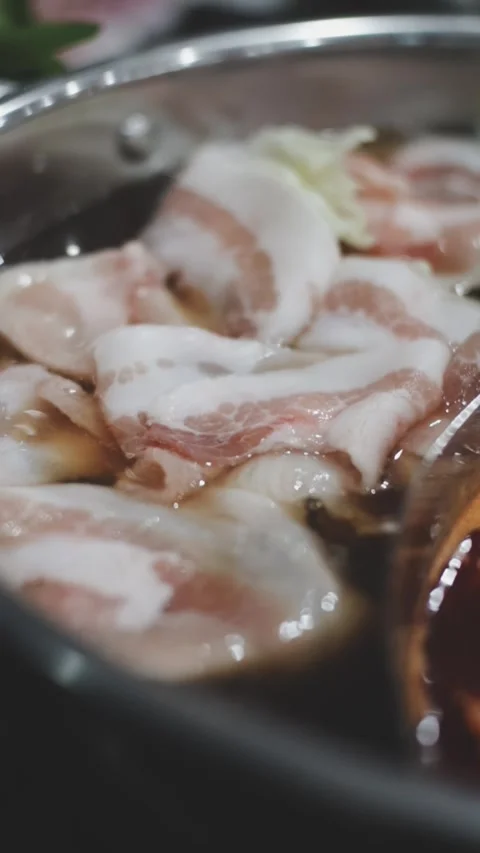 Hands holding chopsticks dipping a slice of pork into a bubbling shabu-shab.. Видео 343613965