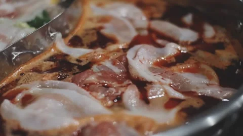 Hands holding chopsticks dipping a slice of pork into a bubbling shabu-shab.. Stock Footage 343613973