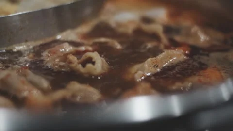 Hands holding chopsticks dipping a slice of pork into a bubbling shabu-shab.. Vidéo 343614001