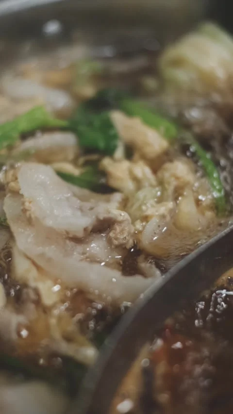 Hands holding chopsticks dipping a slice of pork into a bubbling shabu-shab.. Stock Footage 343614013