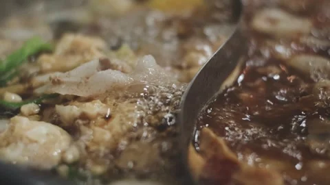 Hands holding chopsticks dipping a slice of pork into a bubbling shabu-shab.. Stock Footage 343614022
