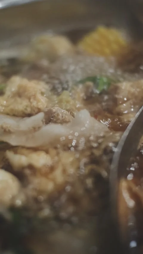 Hands holding chopsticks dipping a slice of pork into a bubbling shabu-shab.. Stock Footage 343614039
