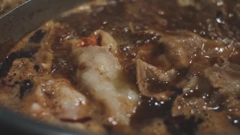 Hands holding chopsticks dipping a slice of pork into a bubbling shabu-shab.. Stock Footage 343614041