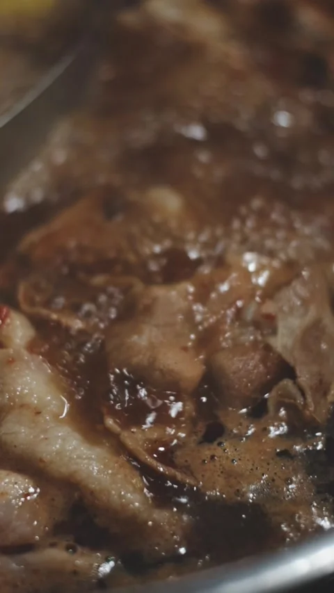 Hands holding chopsticks dipping a slice of pork into a bubbling shabu-shab.. Stock Footage 343614055