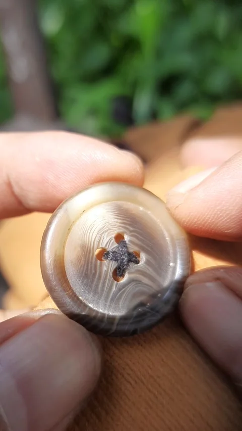 Hands holding circular button, shiny plastic fastener on brown fabric, vert.. Stock Footage 342627289