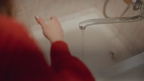 Hands holding clear glass under chrome faucet above porcelain sink, moving Stock Footage 346640599